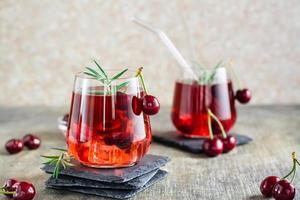 cóctel de cerezas frescas con romero y hielo en vasos sobre la mesa. cócteles sin alcohol caseros foto