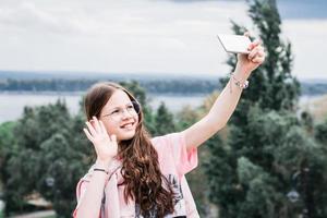 una chica alegre con gafas saluda por videollamada en un smartphone. contenido para redes sociales foto