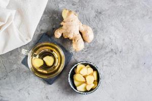 té de jengibre en una taza y raíz picada en un bol sobre la mesa. vitaminas naturales vista superior foto