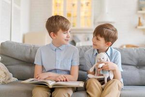 Two boys sitting on couch are reading book. Older brother reads interesting photo