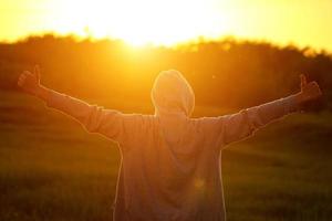 un hombre a la luz de la puesta de sol con las manos en alto, el concepto de éxito, libertad y alegría foto