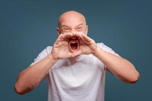 Handsome happy man wearing white T-shirt, guy speaking loudly, isolated on blue background photo