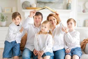 la familia feliz está sentada en una casa nueva en la sala de estar en el sofá sosteniendo un libro foto