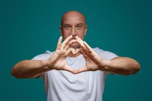 retrato de un hombre calvo sonriendo y tomándose de la mano en forma de corazón, sobre un fondo azul. el concepto de romanticismo foto