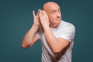 a man on a blue background in holding his hands near his ear, eavesdropping photo