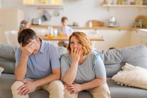 Tense parents sitting on sofa tired crazy loud hyperactive little kids photo