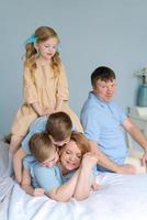 Happy young mother lies on bed in chaos with three young children, two wild photo