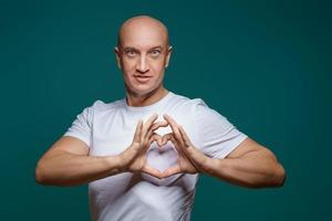 retrato de un hombre calvo sonriendo y tomándose de la mano en forma de corazón, sobre un fondo azul. el concepto de romanticismo foto