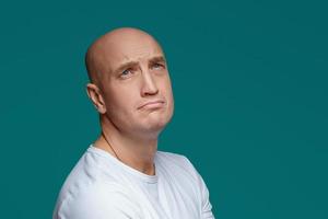 Portrait of a bald adult man with a sad expression in a white t shirt on a blue background photo