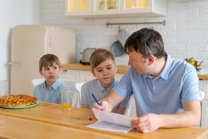 Caring caucasian father sitting at table with his sons and helping photo