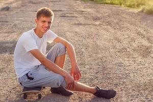 cheerful guy sitting on a skateboard on the road on a Sunny day photo