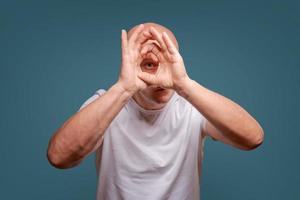 a man on a blue background in holding hands near his eyes like a telescope Peeps photo