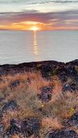 Pan up from rocks and grass to reveal sun setting over water video