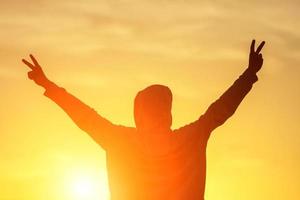 a man in the light of the sunset with his hands up, the concept of success, freedom and joy photo