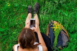 mujer sentada en la hierba verde con el teléfono en la vista superior de la mano foto