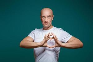 Portrait of a bald man smiling and holding hands in the shape of a heart, on a blue background . The concept of romance photo