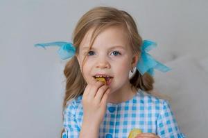 retrato feliz niña caucásica comiendo papas fritas crujientes en gris foto