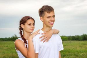 joven hermosa pareja linda chica y chico están de pie del brazo en un fondo de la naturaleza, el concepto de la relación foto