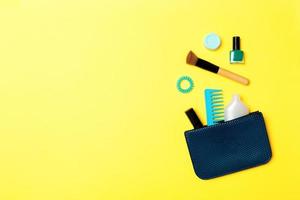 Make up products spilling out of cosmetics bag on yellow background with empty space for your design photo