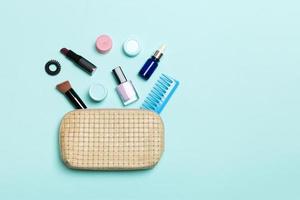 vista superior del conjunto de productos de maquillaje y cuidado de la piel que se derraman de la bolsa de cosméticos sobre fondo azul. concepto de belleza foto