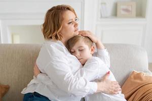 Happy young mom hugs her toddler son, relaxing on sofa at home. Cute toddler photo