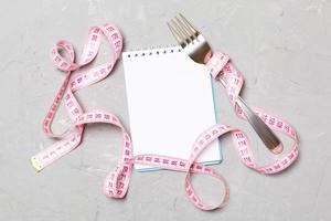 Pink measure tape, open notebook and fork on cement background with empty space for your idea. Top view of healthy lifestyle concept photo