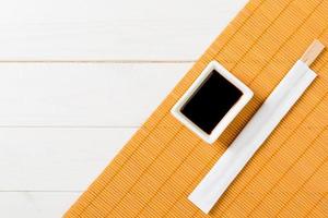 Bamboo mat and soy sauce with sushi chopsticks on white wooden table. Top view with copy space background for sushi. Flat lay photo