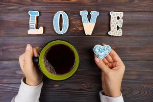manos femeninas con café y galletas en forma de corazón sobre una mesa de madera, vista superior. concepto de amor foto