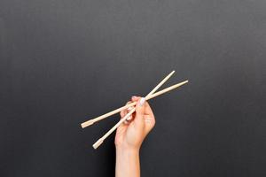 Female hand holding chopsticks on black background. Sushi concept with empty space for your idea photo