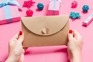 Top view of woman holding an envelope on pink background made of holiday decorations. Christmas time concept photo