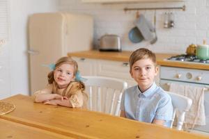 Children sit at table in kitchen and wait for their parents to make them photo