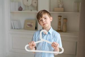 Little caucasian boy is holding hanger in room against background wall photo