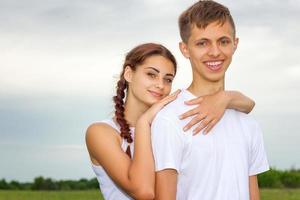 joven hermosa pareja linda chica y chico están de pie del brazo en un fondo de la naturaleza, el concepto de la relación foto