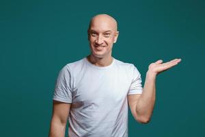 Portrait of a bald cheerful man holding his hand to the side shows a gesture to the side, copy space photo