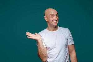 Portrait of a bald cheerful man holding his hand to the side shows a gesture to the side, copy space photo