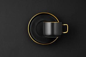 A set of black and golden ceramic plates and cup on a black background. Top view photo