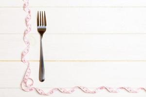 Fork surrounded with curled tape measure on wooden background with copy space. Top view of proper diet concept photo