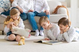 Happy caucasian parents sit relax on sofa and watch as busy little children lie photo