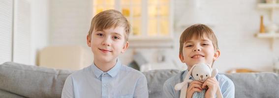 Boys are reading book while sitting on couch at home. Brothers read book. Older photo