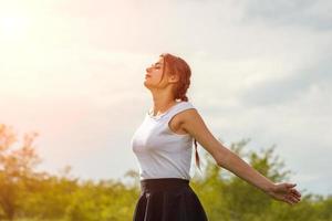 beautiful girl enjoying the sun with her arms outstretched in the field against the sky photo