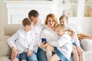 Happy parents with three kids using smartphone at home together sitting on cozy photo