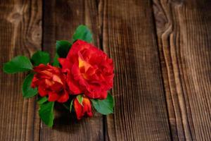 A small vase of red roses on a wooden table. photo