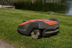 Robotic Lawn Mower on green grass background.Automatic robot lawnmower in modern garden.Green grass trimming with lawn mower. Close-up view of the lawn mower dirty blade after mowing the lawn. photo