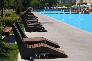 A recreation and relaxation area by the pool in a hotel or a fountain in a park. Row of water jets in a modern fountain, blue water. Streams flowing out of the tube. Summer cityscape. photo