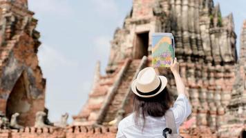 mujer alegre vagabunda con aspecto moderno buscando dirección en el mapa de ubicación mientras viaja al templo foto