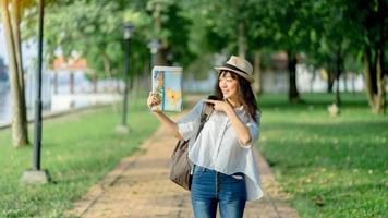 turista hipster con camisa blanca y sombrero sosteniendo un mapa para buscar la dirección en el mapa de ubicación foto