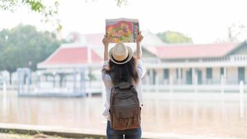 Young woman traveler with backpack and hat looking the map with temple Thailand background photo