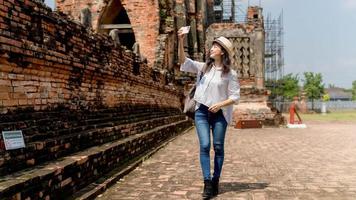 Beautiful young woman wearing white shirt and hat taking photo by mobile in temple ayutthaya thailand, Travel Holiday Relaxation Concept