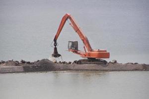 The crane stands on the artificial coast pours sand on the artificial river bank. photo