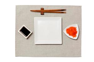 Empty white square plate with chopsticks for sushi, ginger and soy sauce on grey napkin background. Top view with copy space for you design photo